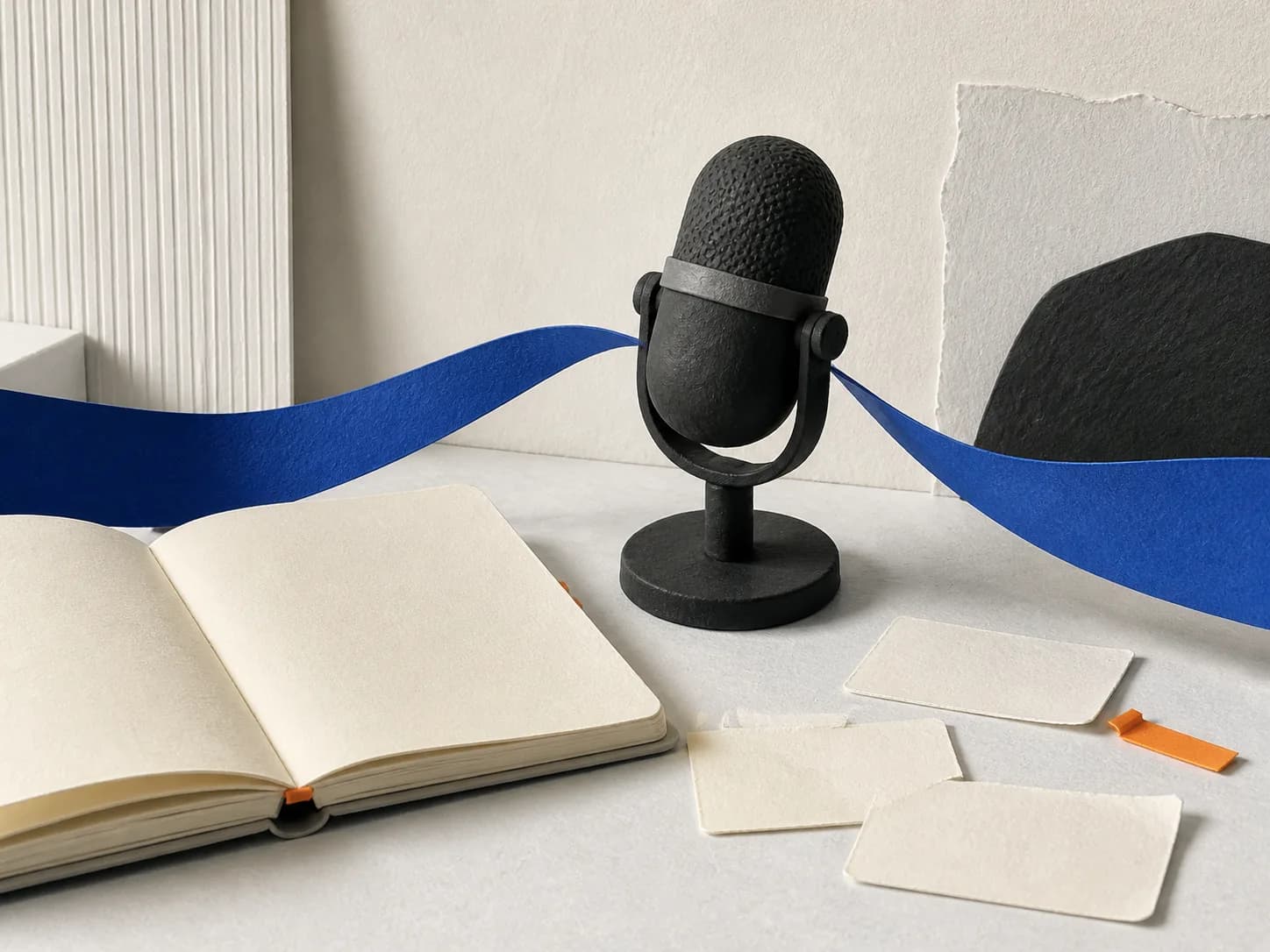 A paper-and-clay microphone beside a blank notebook, prompt cards, and a cobalt ribbon.
